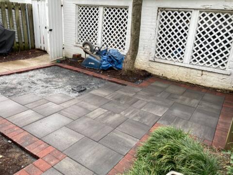 Paver patio installation in progress with grey concrete pavers, red brick border, and garden area at Tenleytown Lawn & Landscape.