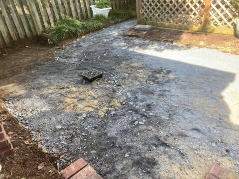 Uneven gravel and dirt garden pathway under renovation, surrounded by wooden fencing and garden plants.