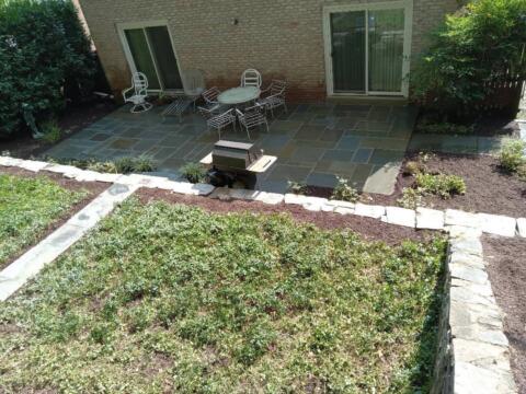 Outdoor patio with stone paving, garden furniture, and lush greenery.