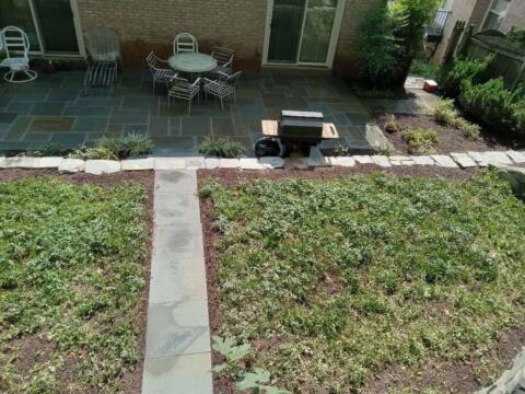 Lush backyard garden with patio and outdoor dining area featuring stone pathway and greenery.