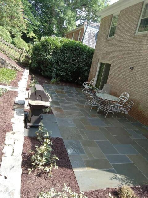 Colorful stone patio with outdoor dining area and manicured garden at the backyard.