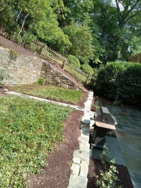 Lush green landscape with stone retaining wall and garden bed, showcasing professional residential landscaping.