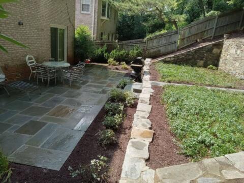 Stone patio with outdoor furniture and lush garden bed at the back of a house.
