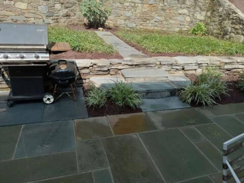 Stylish stone patio with lush plants and steps leading to a landscaped garden area.