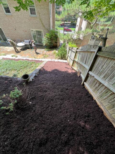 Fresh wood mulch being spread along a backyard fence line.