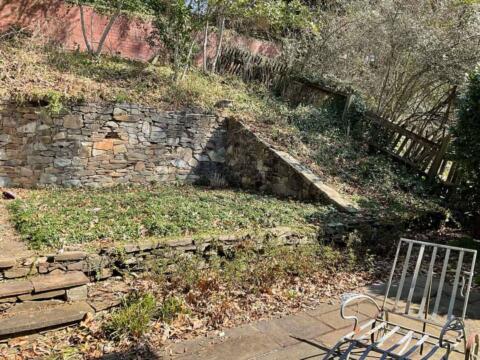 Lush backyard with stone retaining wall, greenery, and outdoor seating area in autumn.