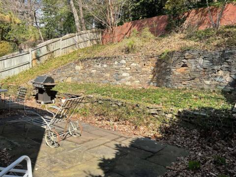 Varied stone retaining walls behind a patio with outdoor furniture and barbecue grill.