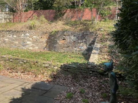 Weathered stone retaining wall in a backyard garden with a stone pathway and a garden statue; landscaping and garden maintenance.