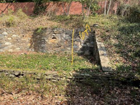 Cracked stone retaining wall with yellow markings in the backyard.