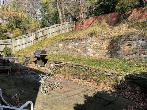 Lush backyard garden with stone retaining wall and outdoor seating area, perfect for relaxation and entertaining.