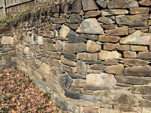 Uneven stone retaining wall with natural slate stones and dry stacking design.