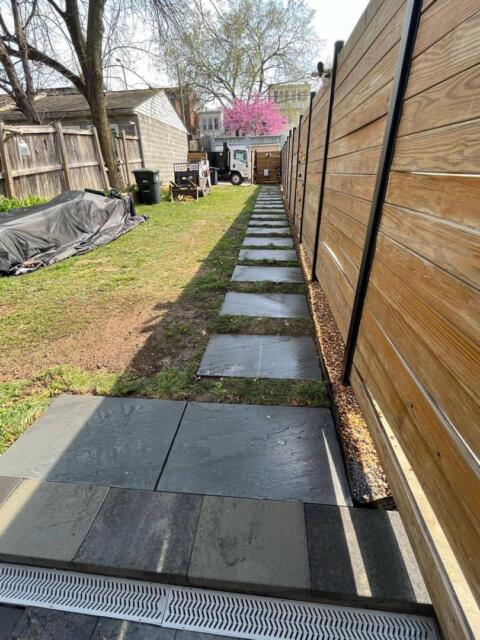 Durable gray stone walkway along wooden fence in backyard.