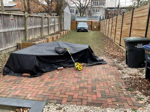 Covered outdoor furniture on a brick patio in a residential backyard.