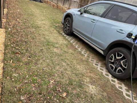 Electric vehicle charging station on a residential lawn with a parked car connected to a charger.