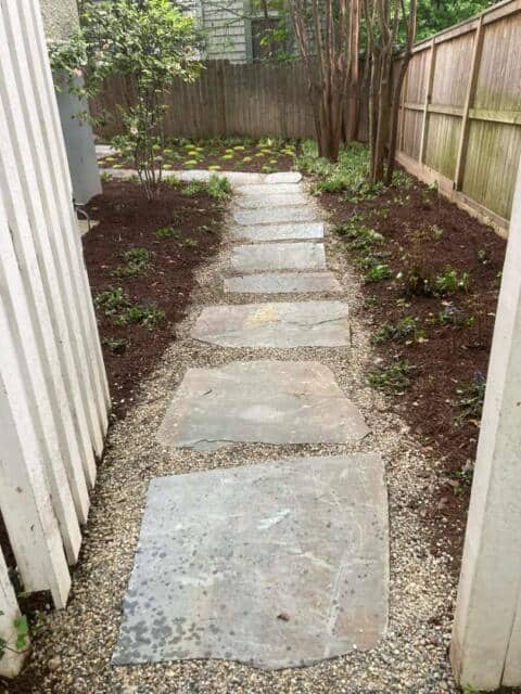 Natural stone pathway in a backyard garden with flower beds and wooden fences.