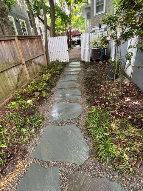 Natural stone pathway in a backyard garden with lush greenery and wooden fencing.