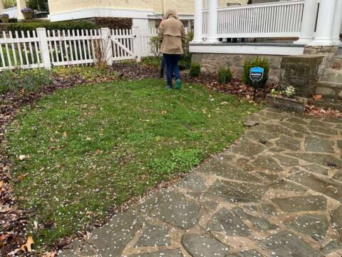 Lawn care with a person tending to a lush green yard near a white porch fence.