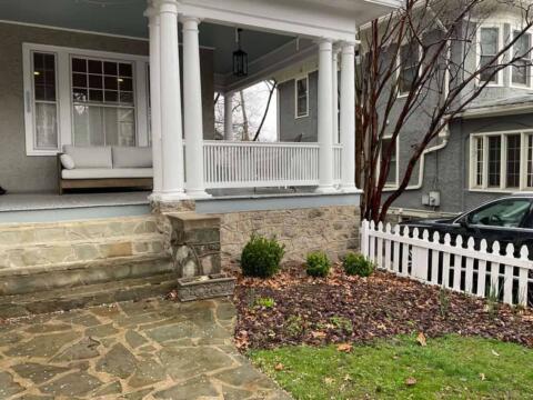 Stylish front porch with white columns, a cozy seating area, and well-maintained landscaped garden.