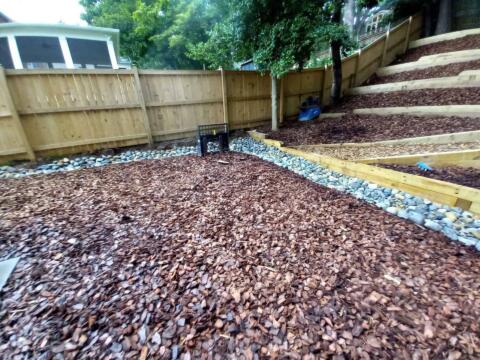 Selected rock and wood landscaped backyard incorporating tiered planting beds and decorative stones.
