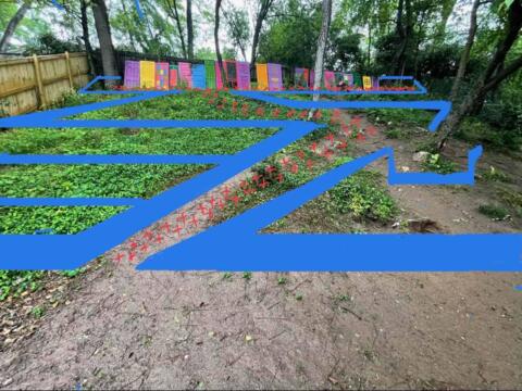 Colorful garden decorations displayed along a lush, fenced backyard landscape.