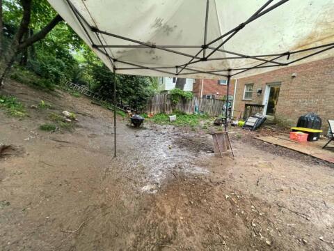 Untidy backyard with dirt ground, tools, and supplies beneath a canopy, showing landscape cleanup efforts.